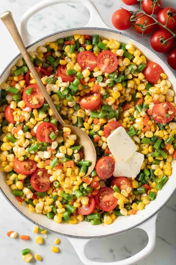 Succotash Recipe Succotash in a white skillet with a serving spoon.