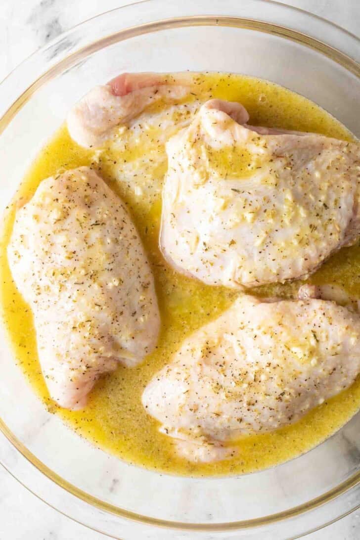 Garlic Lemon Marinade For Chicken Chicken thighs and lemon garlic chicken marinade in a clear glass bowl.