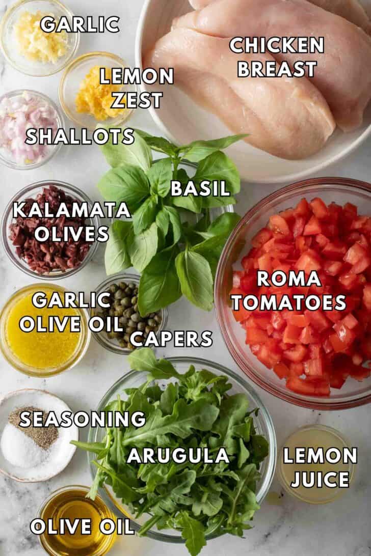Bruschetta Chicken Recipe Clear glass bowls filled with arugula, chopped Roma tomatoes, chicken cutlets, kalamata olives and olive oil for a Bruschetta Chicken recipe.