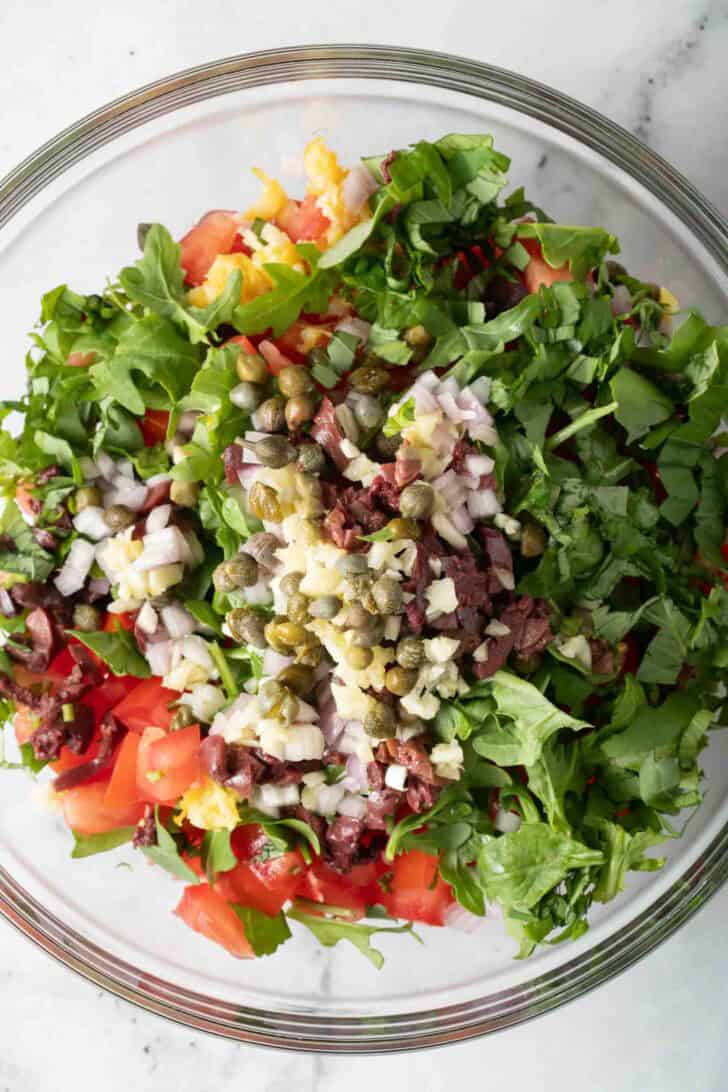 Bruschetta Chicken Recipe A clear glass bowl filled with chopped arugula, Roma tomatoes, onion, garlic and kalamata olives for an Italian Salsa.