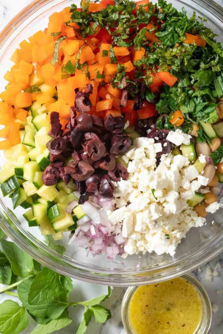 How to Make Greek Dense Bean Salad Dense Bean Greek Salad ingredients in a clear glass bowl.