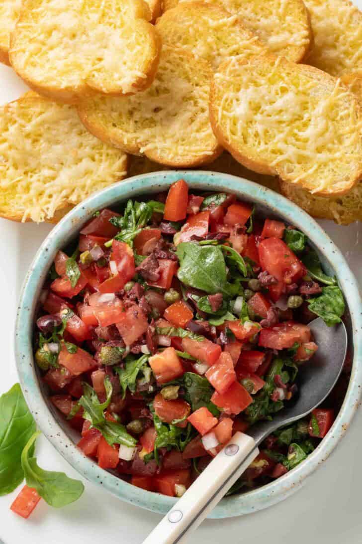 Tomato Bruschetta A bowl of Roma tomatoes for bruschetta on a serving plate next to cheese toasts for a tomato bruschetta recipe.