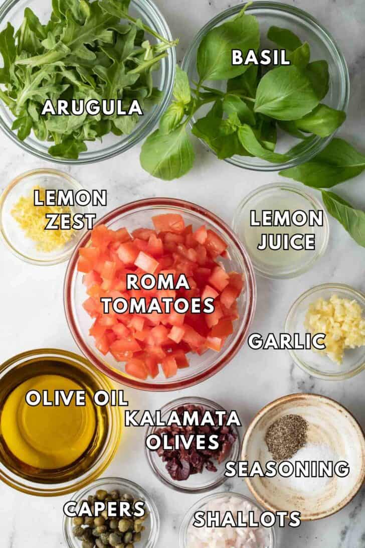 Italian Salsa Recipe Clear glass bowls filled with Roma tomatoes, arugula, basil, kalamata olives, and capers for an Italian Salsa recipe.
