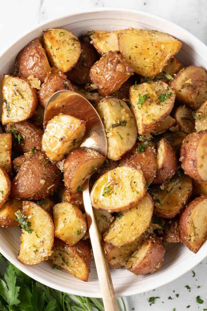 Roasted Red Potatoes With Rosemary Roasted Red Potatoes with rosemary in a white bowl with a serving spoon.