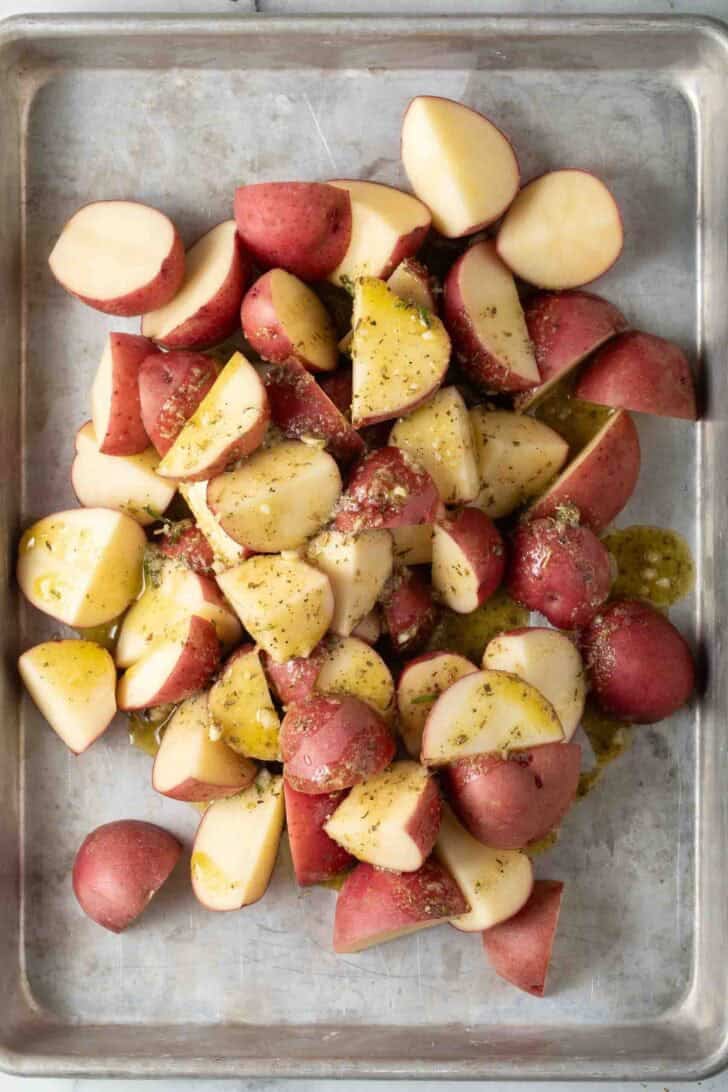 Oven Roasted Red Potatoes Recipe Baby red potatoes cut in half coated with olive oil and seasonings on a baking sheet for Oven Roasted Red Potatoes Recipe.