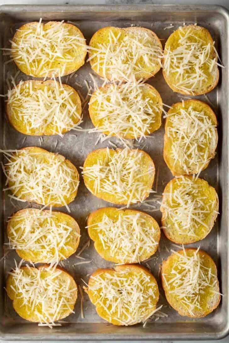 How to Make Bruschetta Slices of baguette brushed with garlic oil and topped with grated parmesan cheese on a baking sheet.