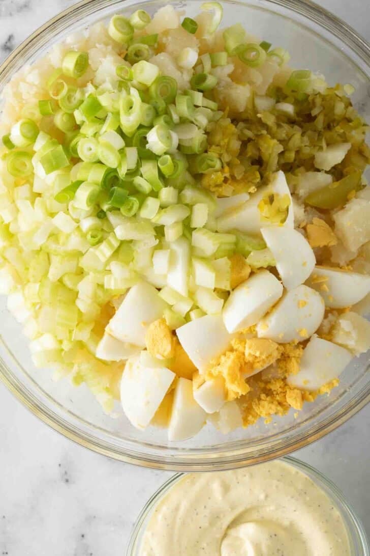 Recipe for Deviled Egg Potato Salad Potato Salad with deviled eggs in a clear glass bowl next to a clear glass bowl of dressing.