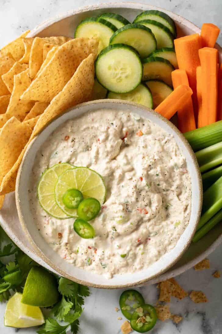Tuna Fish Dip Spicy tuna fish dip in a bowl next to tortilla chips, slices of cucumber, carrot and celery.