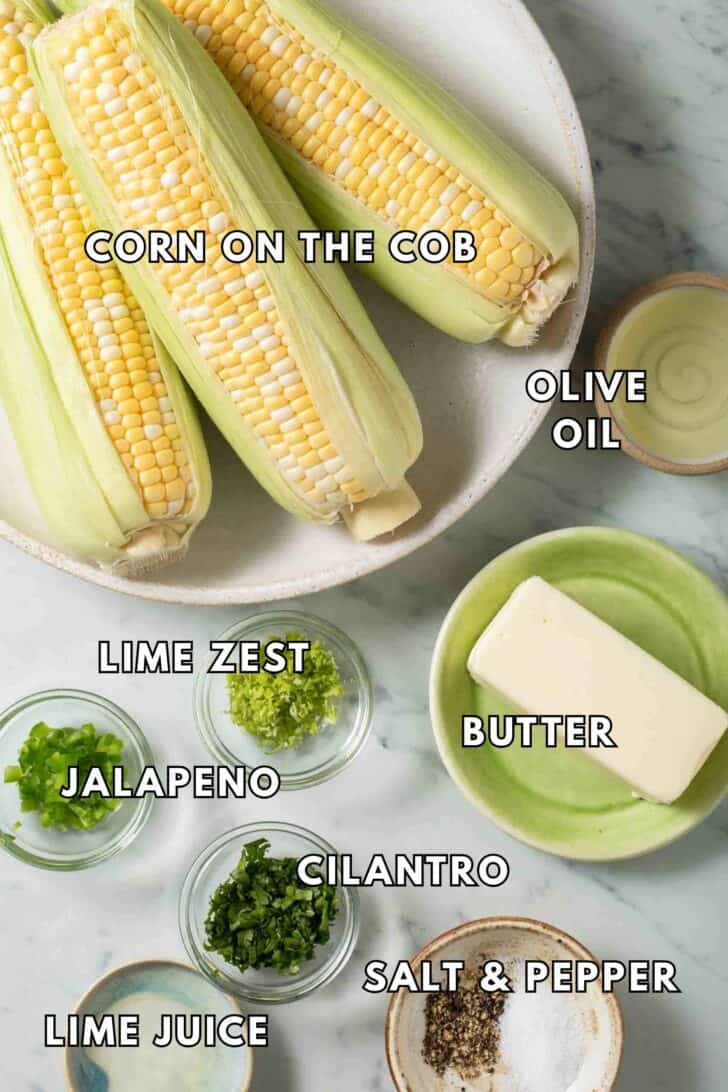 Air Fryer Corn on the Cob Fresh ears of corn on a plate next to butter.