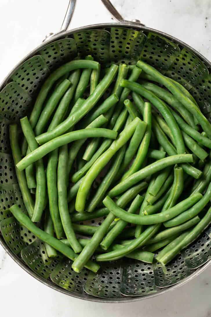 Cold Green Bean Salad Recipe Steamed green beans in a steamer basket for a green bean salad recipe.