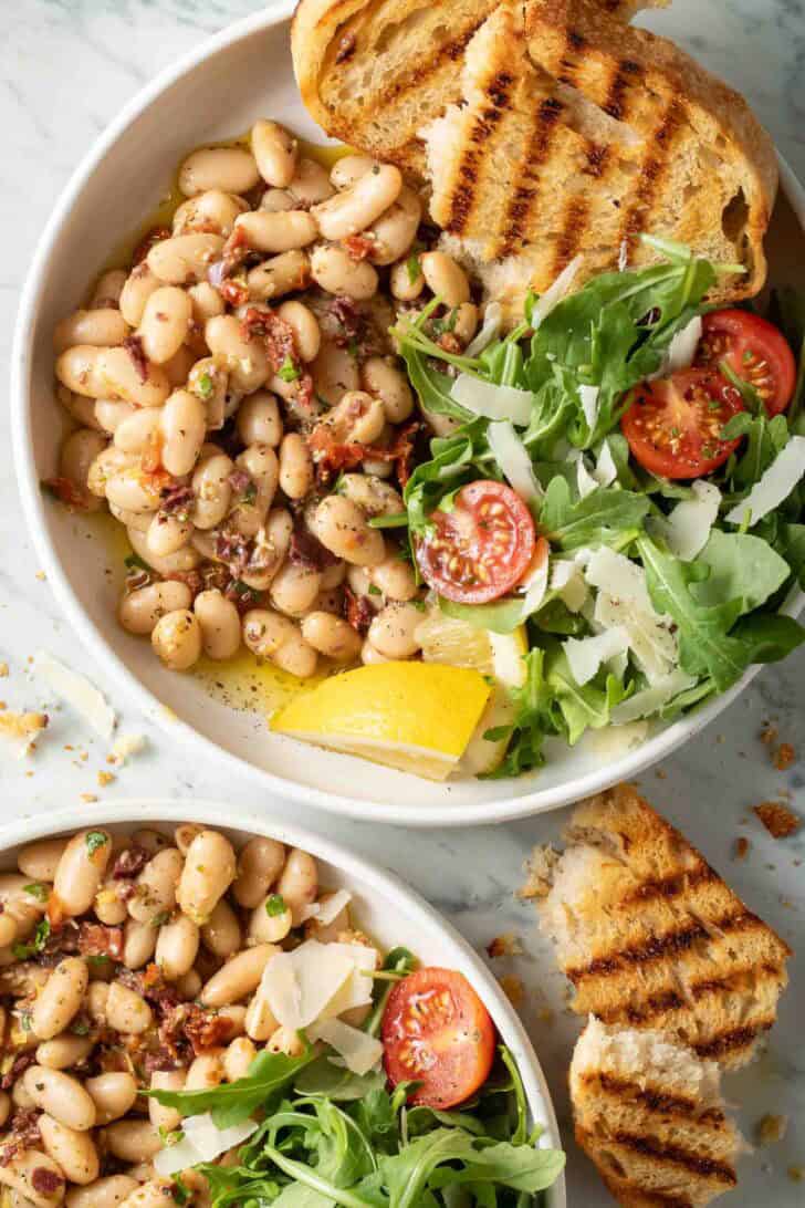 Marinated White Beans Marinated White Beans on a plate with arugula salad and grilled bread.