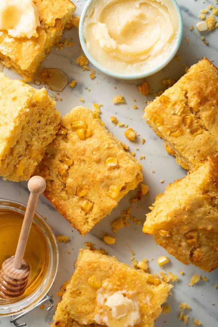 Moist Cornbread Recipe Cut Square Pieces of Southern Cornbread next to a jar of honey and small bowl of butter.