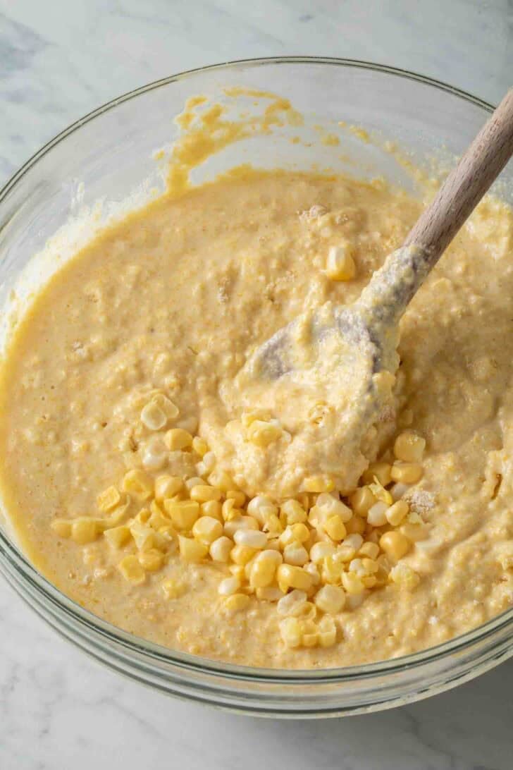 Cornbread From Scratch Cornbread from scratch batter in a clear glass bowl with a wooden spoon.