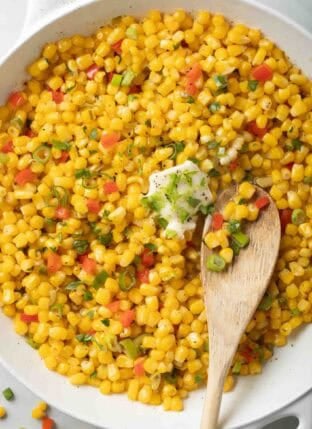 Skillet Corn in a white skillet with a wooden spoon.