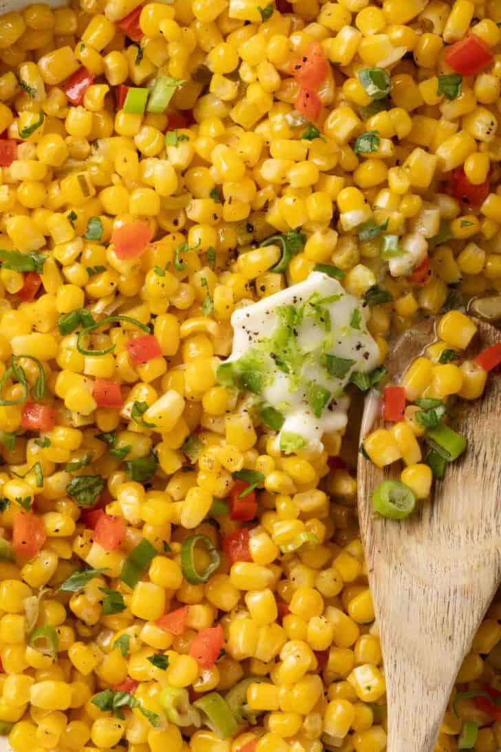 Fried Corn Recipe Fried Corn in a white skillet with a wooden spoon.