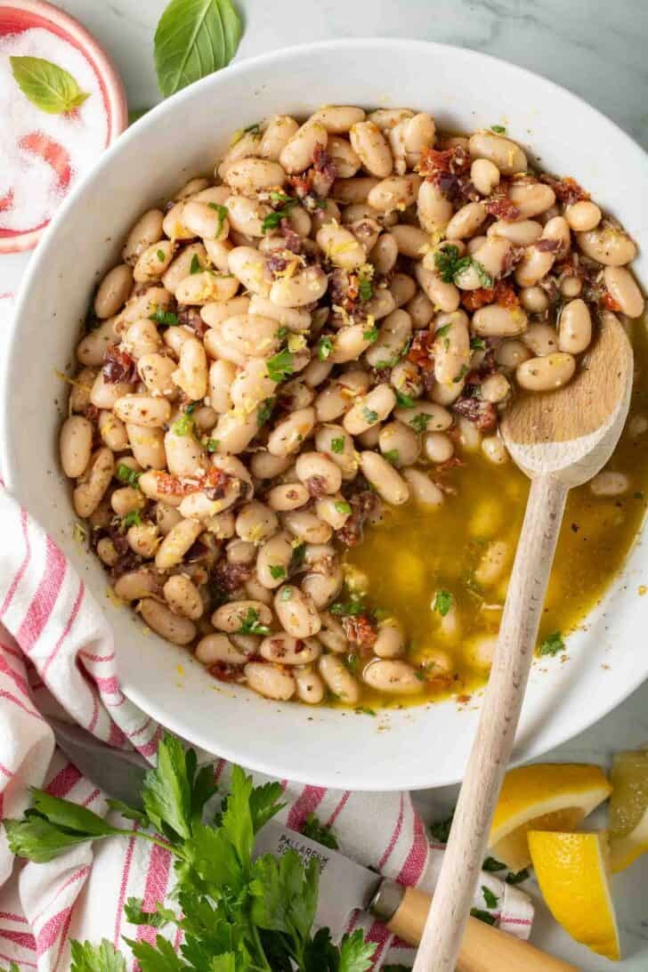 Marinated Cannellini Beans Marinated Cannellini Beans in a white bowl with a wooden spoon.