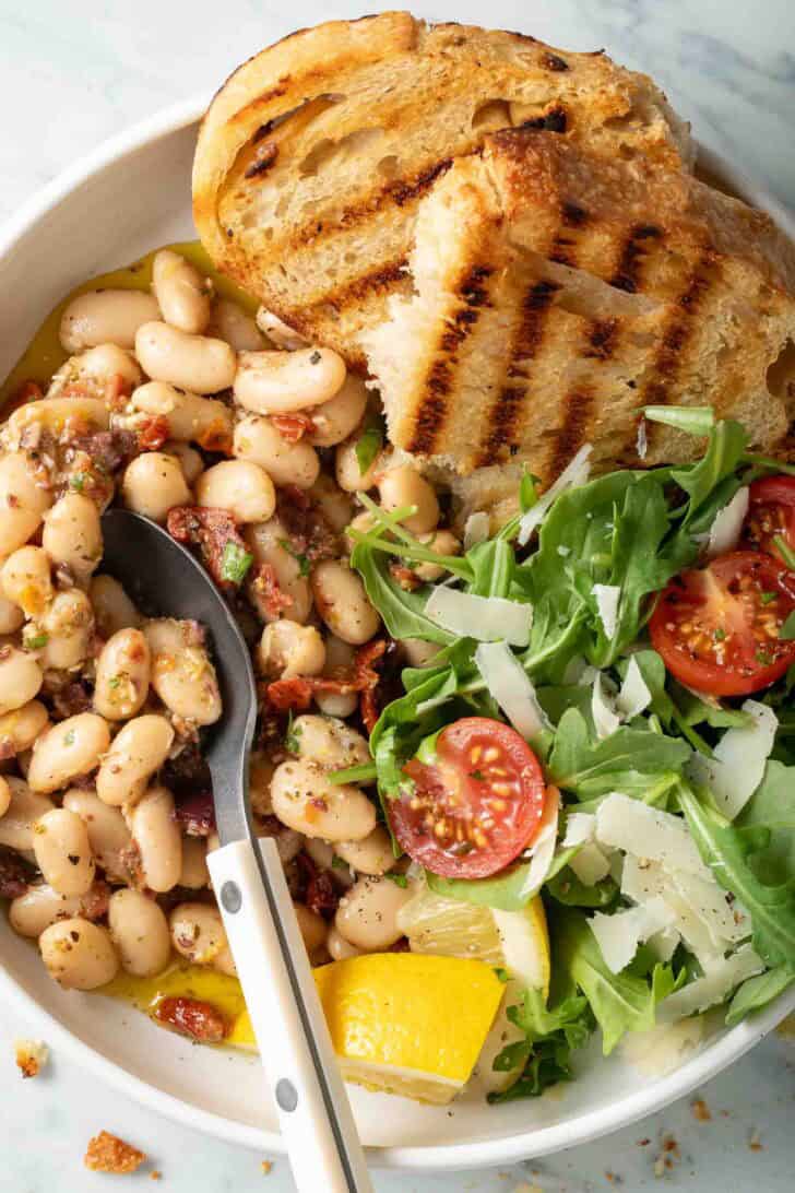 Marinated White Beans Recipe Marinated White Beans on a plate with an arugula salad and grilled bread.