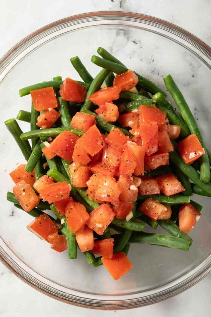 Cold String Bean Salad Steamed green beans and marinated chopped tomatoes in a clear glass bowl.