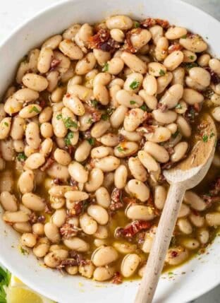 Marinated White Beans in a white bowl with a wooden spoon.