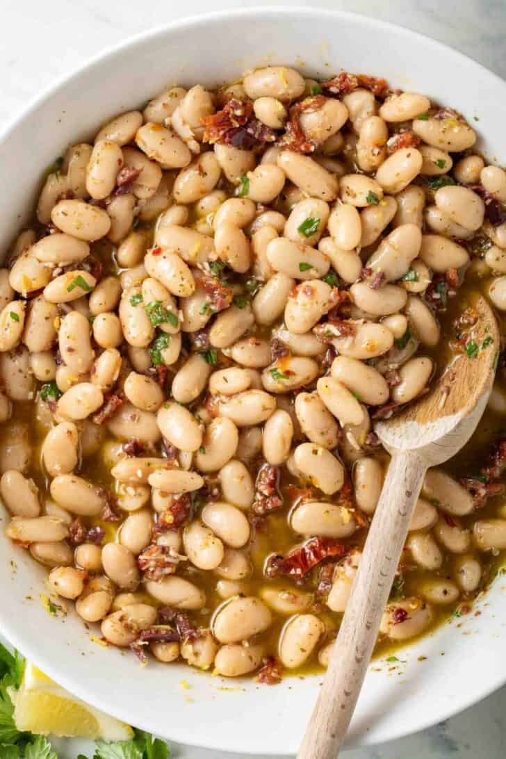 Marinated Beans Marinated Beans in a white bowl with a wooden spoon.