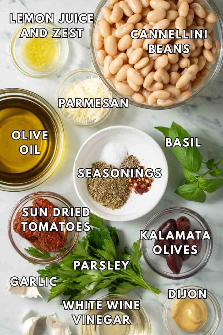 Marinated White Beans Recipe Cannellini beans in a clear glass bowl next to bowls of olive oil, lemon juice, parmesan cheese, and sun dried tomatoes for a Marinated White Beans recipe.