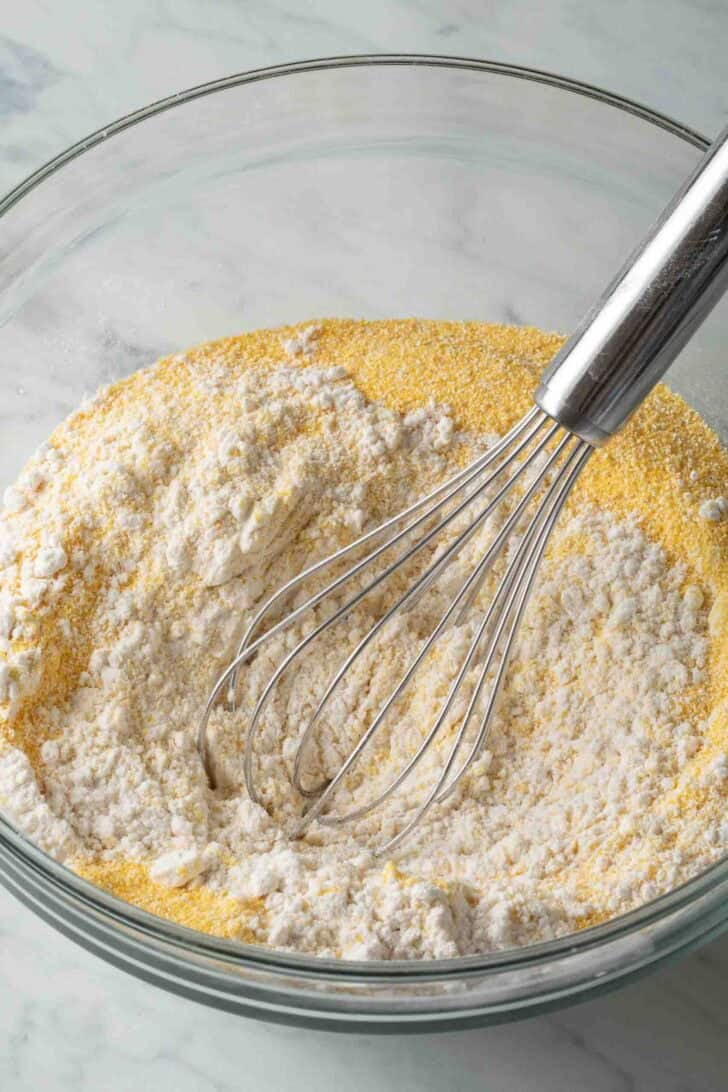 Cornbread From Scratch Corn meal and flour in a glass mixing bowl with a wire whisk.