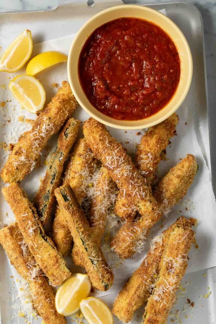 Parmesan Zucchini Fries Parmesan Zucchini Fries on a baking sheet with a bowl of marinara sauce.