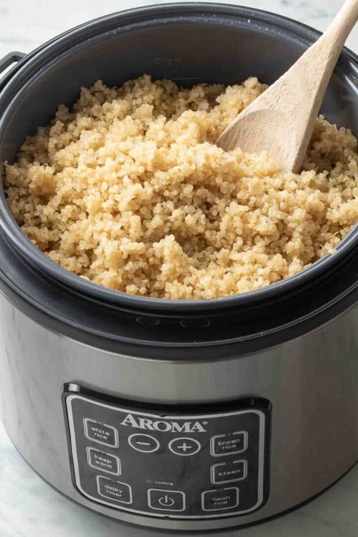 Quinoa in a rice cooker with a wooden spoon.