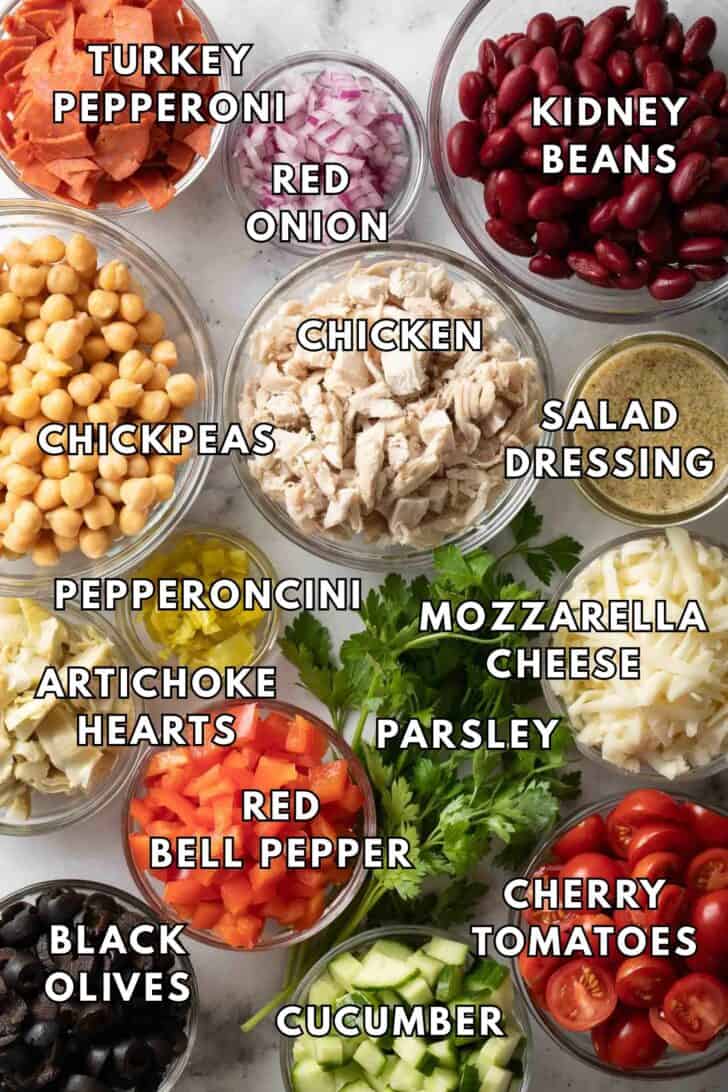 Dense Bean Salad Recipe Clear glass bowls filled with kidney beans, chickpeas, chopped chicken, tomatoes and salad dressing for a Dense Bean Salad recipe.