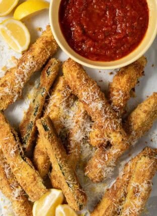 Baked Zucchini Fries on a tray with a bowl of marinara dipping sauce.