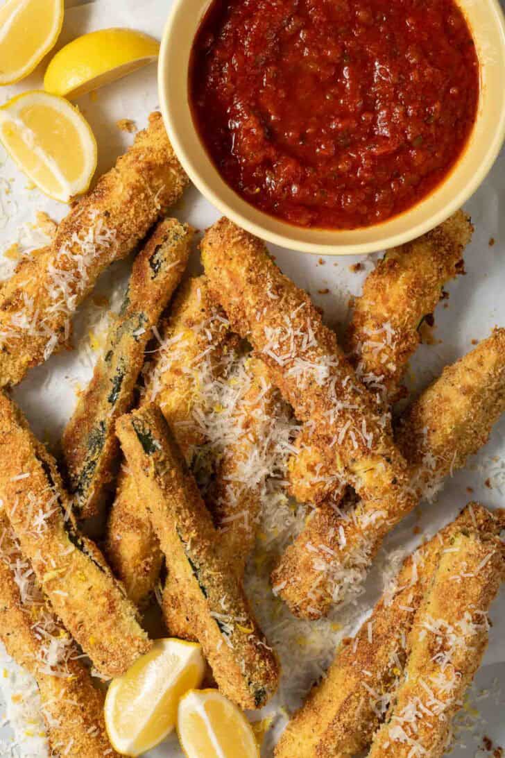 Zucchini Fries Baked Zucchini Fries scattered on a tray with a bowl of marinara dipping sauce.