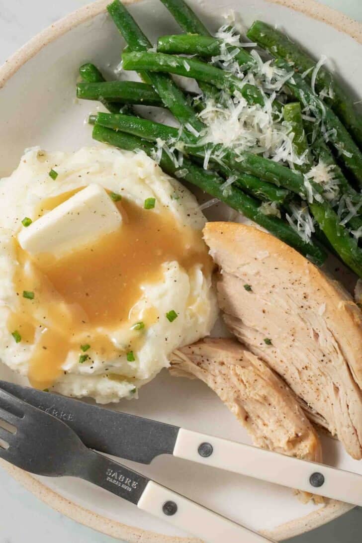 Mashed Potatoes With Sour Cream Mashed Potatoes with Sour Cream with gravy on a plate with sliced turkey and green beans.