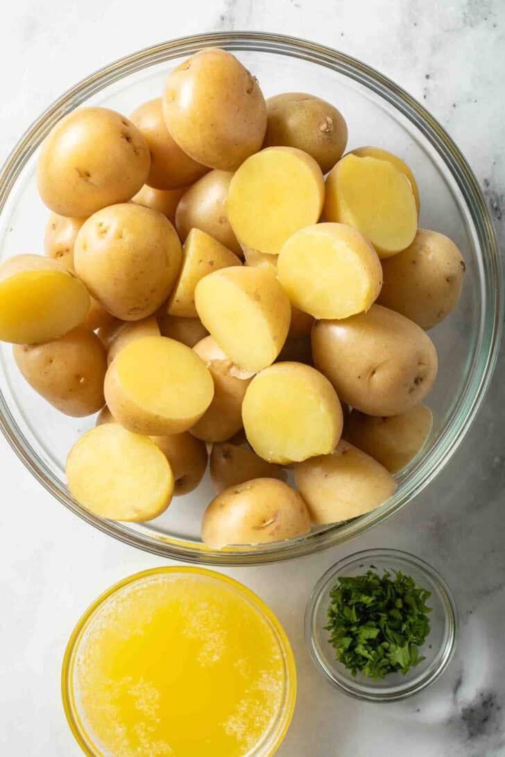 Boil Potatoes Recipe Baby Yukon Gold potatoes in a glass bowl next to a bowl of melted butter for boiled potatoes recipe.