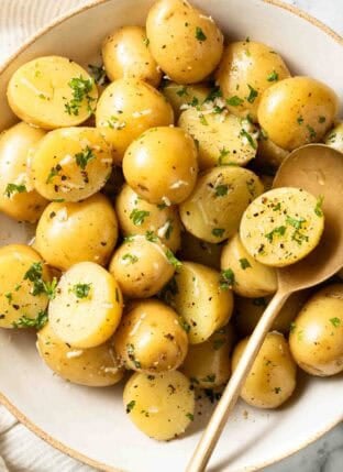 Boiled Potatoes with butter in a white bowl and serving spoon.