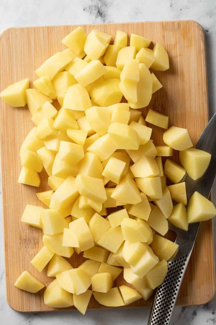 How to Make Garlic Parmesan Mashed Potatoes Cut potatoes on a wooden cutting board with a knife.