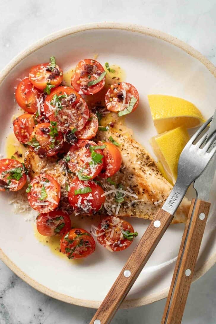 Marinated Tomato Salad Marinated tomato salad over grilled chicken on a white plate.