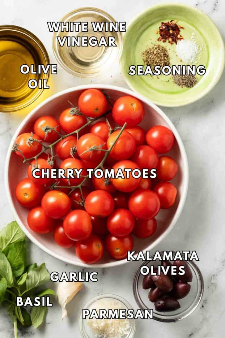 Marinated Cherry Tomatoes Recipe Cherry tomatoes in a white bowl next to bowls of olive oil, vinegar, kalamata olives and parmesan cheese for a marinated cherry tomatoes recipe,.