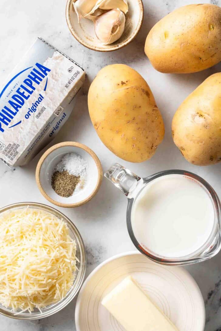 Garlic Parmesan Mashed Potatoes Recipe Yukon gold potatoes, next to cream cheese, butter, milk and grated parmesan cheese for Garlic Parmesan Mashed Potatoes recipe.