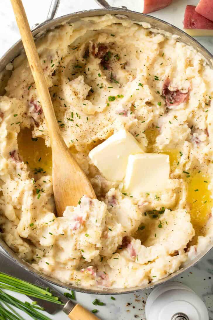Mashed Red Potatoes in a pot with a wooden spoon.