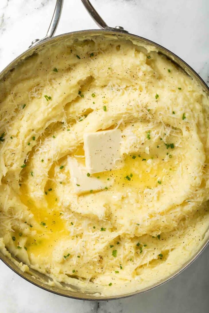 Garlic and Parmesan Mashed Potatoes Garlic and parmesan mashed potatoes in a stainless steel pot with melted butter on top.
