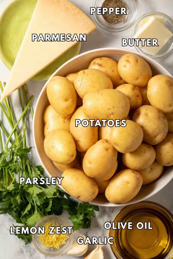 Parsley Potatoes Recipe A bowl filled with baby Yukon gold potatoes next to fresh parsley, olive oil, parmesan cheese and garlic for a Parsley Potatoes recipe.