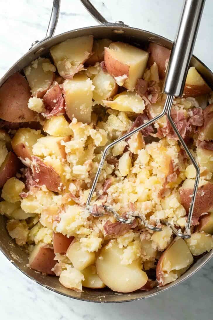 Red Mashed Potatoes in a pot with a hand masher.