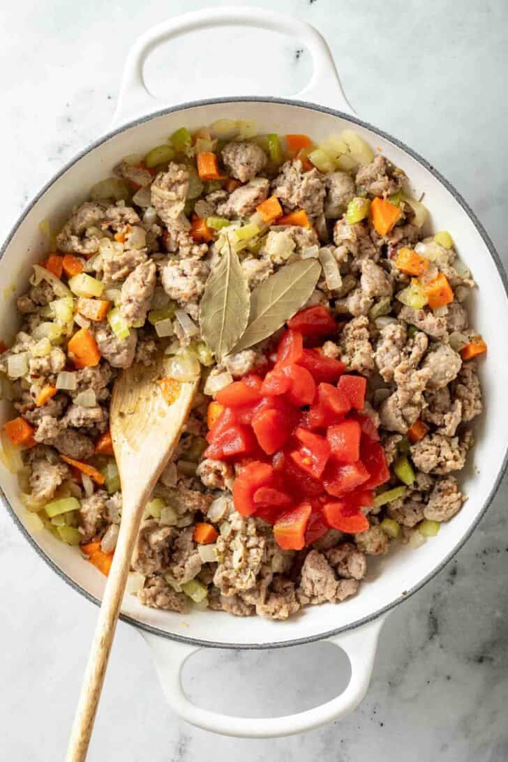 How to Make Creamy Sausage Ditalini Soup Cooked Italian sausage and vegetables in a white pot with canned tomatoes and bay leaves.