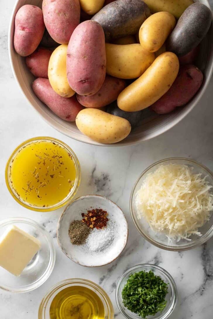 Roasted Fingerling Potatoes Recipe Fingerling potatoes in a white bowl next to olive oil, parmesan cheese and parsley.
