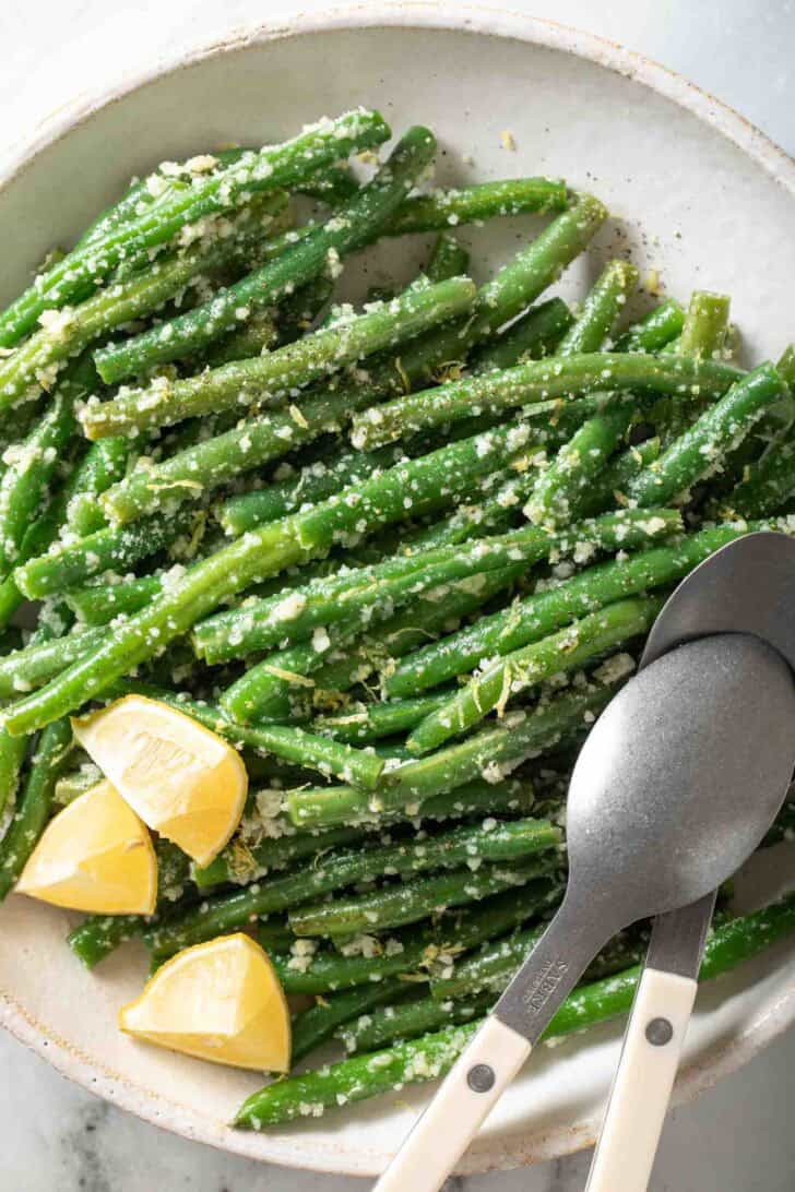 Garlic Green Beans Garlic Green Beans on a white plate with serving spoons.