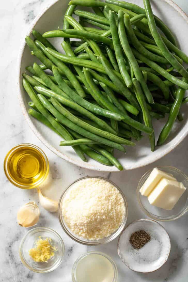 Garlic Green Beans Recipe Fresh green beans on a plate next to ingredients for Garlic Green Beans Recipe.