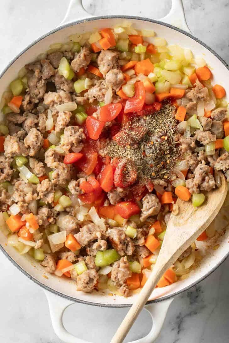Sausage and Vegetable Soup Recipe Cooked crumbled Italian sausage with chopped carrots, celery and onions in a white Dutch oven.