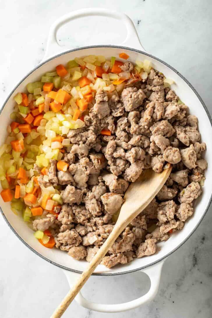 How to Make Creamy Parmesan Italian Sausage Soup Cooked Italian sausage and vegetables in a white pot.