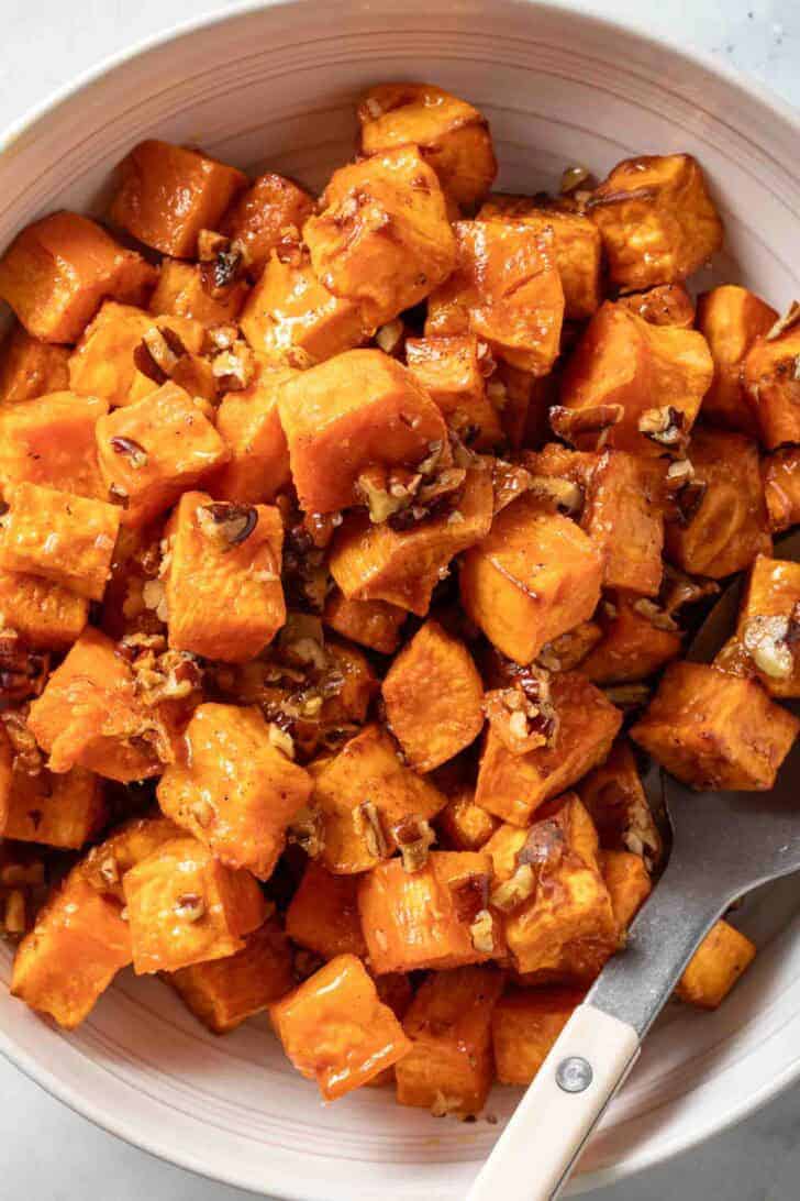 Oven Roasted Sweet Potatoes Oven Roasted Sweet Potato Cubes with pure maple syrup and pecans in a serving bowl.