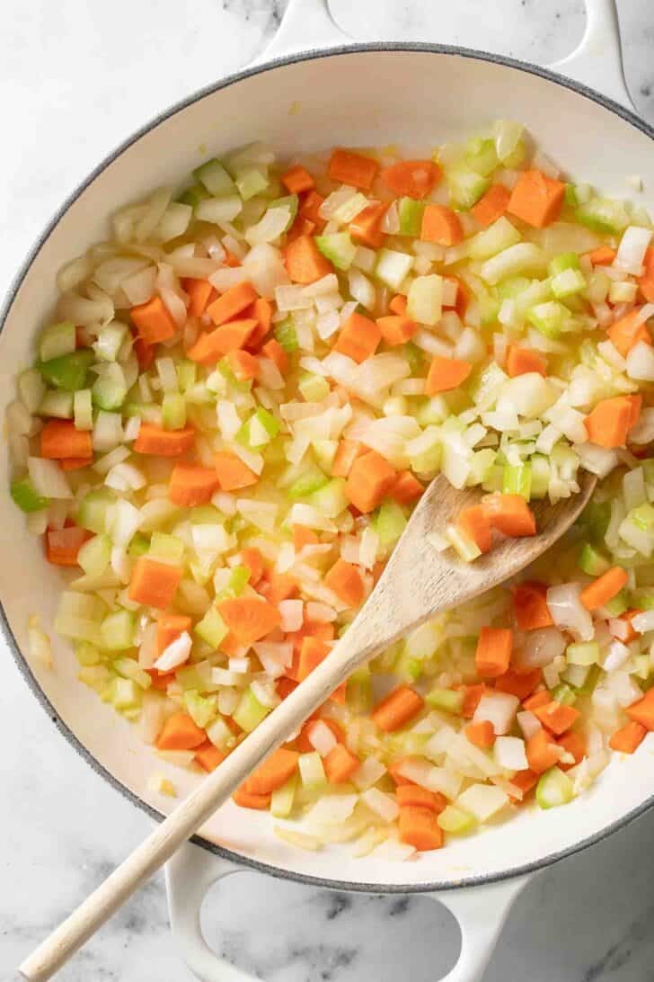 Sausage Vegetable Soup Recipe Chopped carrots, celery and onion in a white Dutch oven for a sausage and vegetable soup recipe.